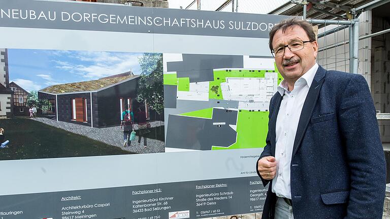 Ein futuristisches Gebäude hat der Architekt als Dorfgemeinschaftshaus für Sulzdorf entworfen. Bürgermeister Friedel Heckenlauer vor der Bautafel. Ein futuristisches Gebäude hat der Architekt als Dorfgemeinschaftshaus für Sulzdorf entworfen. Bürgermeister Friedel Heckenlauer vor der Bautafel.