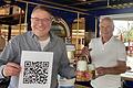 Norbert Bauriedel im Ausschankwagen in Margetshöchheim mit seinem Vater Günter Bauriedel, in der Hand ein QR-Code, der auf die Speisekarte und weitere Informationen führt