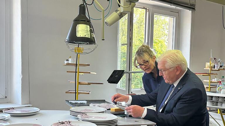 Bundespräsident Steinmeier besucht Porzellanfabrik       -  Bundespräsident Frank-Walter Steinmeier (r) lässt sich bei seinem Besuch der Firma Seltmann in Weiden von Porzellandruckerin Mariella DeLuca die Dekoration eines Tellers erläutern.