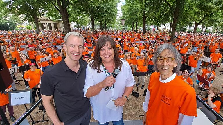Alexander Steinbeis, Intendant des Kissinger Sommers, Susanne Will, Chefin der Saale-Zeitung, und Stardirigent Kent Nagano. Im Hintergrund das Wichtigste: Die rund 600 Musikerinnen und Musiker, die des zweiten Symphonic Mob zu einem Erlebnis macht... - Alexander Steinbeis, Intendant des Kissinger Sommers, Susanne Will(Saale-Zeitung) und Stardirigent Kent Nagano beim Symphonic Mob 2023. Auch der diesjährige 'Mob' zählt zu seinen Höhepunkten im Kissinger Sommer 2024. Im Hintergrund das Wichtigste: Die rund 600 Musikerinnen und Musiker, die den zweiten Symphonic Mob zu einem Erlebnis machten. Alexander Steinbeis, Intendant des Kissinger Sommers, Susanne Will, Chefin der Saale-Zeitung, und Stardirigent Kent Nagano. Im Hintergrund das Wichtigste: Die rund 600 Musikerinnen und Musiker, die des zweiten Symphonic Mob zu einem Erlebnis macht... - Alexander Steinbeis, Intendant des Kissinger Sommers, Susanne Will(Saale-Zeitung) und Stardirigent Kent Nagano beim Symphonic Mob 2023. Auch der diesjährige 'Mob' zählt zu seinen Höhepunkten im Kissinger Sommer 2024. Im Hintergrund das Wichtigste: Die rund 600 Musikerinnen und Musiker, die den zweiten Symphonic Mob zu einem Erlebnis machten.