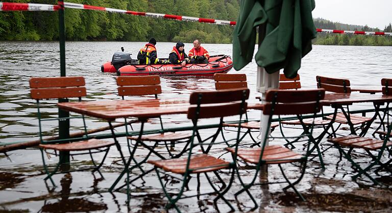 Feuerwehrmänner fahren mit einem Boot über den Deininger Weiher im Landkreis München, der bereits einen Biergarten überflutet hat. Feuerwehrmänner fahren mit einem Boot über den Deininger Weiher im Landkreis München, der bereits einen Biergarten überflutet hat.