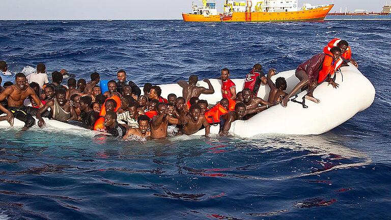 Flüchtlingsboot im Mittelmeer - Flüchtlinge sitzen auf dem Mittelmeer in einem sinkenden Schlauchboot. Die wenigsten tragen eine Rettungsweste. Studenten der FHWS wollen das ändern. Sie haben die „Ein-Euro-Rettungsweste“ entwickelt. Ziel ist es, eine Million Westen an Flüchtlinge im Mittelmeerraum zu verteilen. Bei dem Foto handelt es sich um eine undatierte Aufnahme im Gewässer vor der Insel Lampedusa. Flüchtlingsboot im Mittelmeer - Flüchtlinge sitzen auf dem Mittelmeer in einem sinkenden Schlauchboot. Die wenigsten tragen eine Rettungsweste. Studenten der FHWS wollen das ändern. Sie haben die „Ein-Euro-Rettungsweste“ entwickelt. Ziel ist es, eine Million Westen an Flüchtlinge im Mittelmeerraum zu verteilen. Bei dem Foto handelt es sich um eine undatierte Aufnahme im Gewässer vor der Insel Lampedusa.