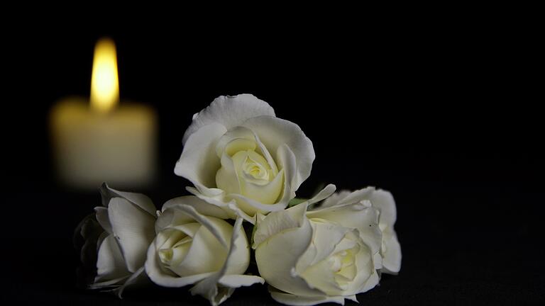 Beautiful White roses with a burning candle on the dark background. Funeral flower and candle on table against black background with copy space.       -  Unternehmen können mit einem Nachruf in der Tageszeitung ihren Mitarbeitern die letzte Ehre erweisen.