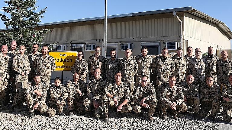 Resolute Support       -  Im Camp Marmal hat sich Oberstleutnant Frank Dannenberg (links) mit einem Teil seiner Soldaten um einen Weihnachtsbaum und um das Ortsschild von Volkach versammelt, welches er vom Volkacher Bürgermeister Peter Kornell mit auf die Reise bekam.