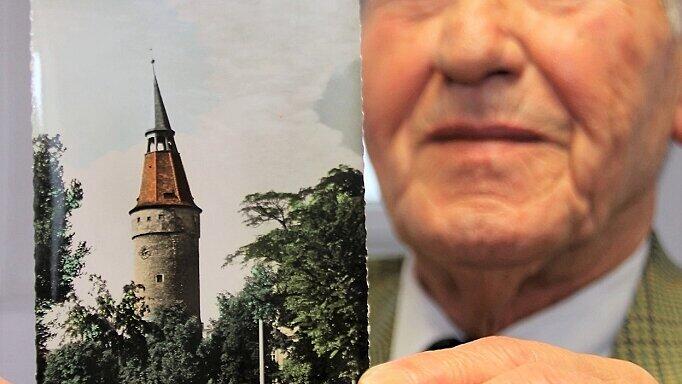 Bruno Grasser zeigt ein Foto aus den 1950er-Jahren, auf dem seine kleine Schwester Hannelore, sein Vater Fritz Grasser und dessen Vorgängerin in der Buchhandlung und Buchbinderei, Frau Berger, vor dem Falterturm auf einer Bank sitzen.