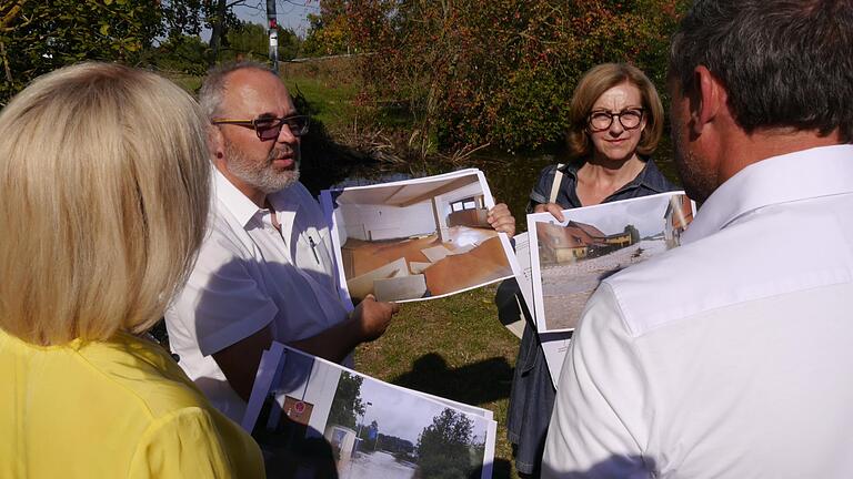 Der Schwarzacher Bürgermeister Volker Schmitt (FW) zeigt direkt am Ufer der Schwarzach auf Fotos die Ausmaße des Hochwassers im Juli. Rechts im Bild Susanne Knof (FW), Bürgermeisterin des ebenfalls vom Hochwasser betroffenen Obernbreit.