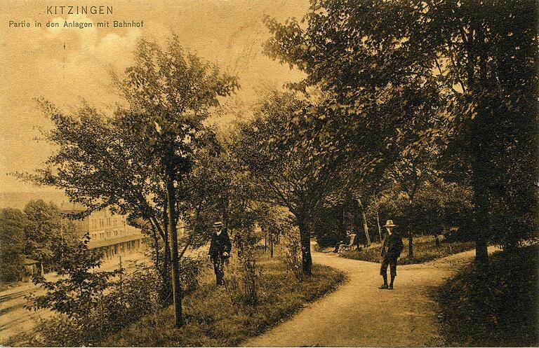 Die Postkarte von 1906 zeigt zwei Spaziergänger in der Grünanlage und am linken Rand den Kitzinger Bahnhof.