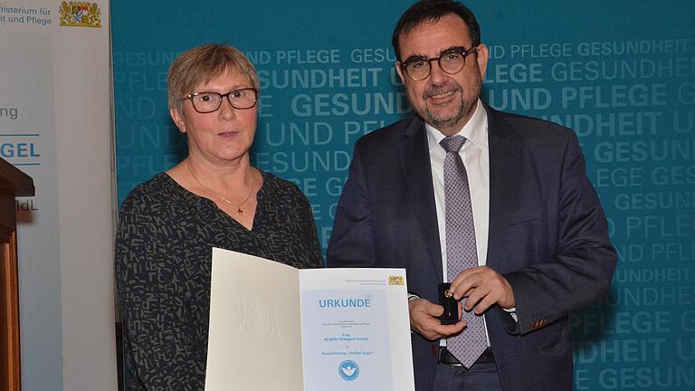 Brigitte Unrath mit ihrer Urkunde und Minister Klaus Holetschek. Brigitte Unrath mit ihrer Urkunde und Minister Klaus Holetschek.