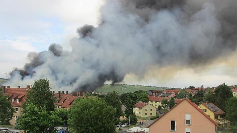 Zuckerfabrik: Brandgeruch hängt noch in der Luft - Es ist Montagvormittag, und noch immer liegt in der Marktbreiter Straße ein leicht brenzliger Geruch in der Luft. Abgesehen von dem Geruch aber erinnert zwei Tage nach dem Großbrand auf dem Gelände der Zuckerfabrik kaum noch etwas an das Wüten des Feuers am Samstagabend. Gesprächsthema ist der Brand in Ochsenfurt jedoch nach wie vor – besonders im Bärental, wohin der Wind den dichten Rauch getrieben hatte.
„Eine Stunde zuvor sind wir am Samstag noch an der Zuckerfabrik vorbei gelaufen“, erzählt Gerlinde Steiner. „Da war gar nichts.“ Sie wohnt unterhalb der Main-Klinik und kommt auf dem Weg zum Einkaufen häufig am Werksgelände vorbei. Als sie aus ihrem Fenster die schwarzen Wolken den Berg hinauf ziehen sah, dachte sie noch, es brenne irgendwo weiter unten im Bärental. „Ich habe gleich die Fenster zugemacht, denn es roch extrem beißend“, sagt die Anwohnerin. Ihr Mann, erzählt sie, habe sofort auf die Strohballen an der Zuckerfabrik als Brandherd getippt. Dass die provisorische Lärmschutzwand in Flammen aufgegangen war, sprach sich in der Nachbarschaft sofort herum. Eine leise Sorge beschlich Gerlinde Steiner, als glimmende Kleinteile auf ihr Haus zuflogen. Es habe sich wahrscheinlich um brennende Strohteilchen gehandelt, die von der Hitze des Feuers in die Höhe gerissen wurden, vermutet sie. Reste davon fand das Ehepaar Steiner am Sonntagmorgen auch noch auf dem Balkon. „Das haben wir weggekehrt, und dann war es gut.“ Bis nach Mitternacht habe sie am Samstag die Fenster geschlossen gehalten, berichtet Gerlinde Steiner weiter. Inzwischen könne sie aber keinen Rauchgeruch mehr in ihrer Wohnung wahrnehmen. Bei Peter Polifka dagegen ist auch am Montagmorgen noch ein leichter Rauchgeruch in der Wohnung bemerkbar. Er wohnt am Greinberg und war zu dem Zeitpunkt des Brandes zu Hause. Seine Frau entdeckte die Rauchwolken, als sie nach draußen sah. Er erzählt, dass sie das Geschehen im Internet verfolgten und die Fenster schlossen, sobald der Qualm sich weiter entwickelte. „Direkten Rauch hatten wir zum Glück nicht in der Wohnung. Andere hat es da sicher schlimmer erwischt“, erinnert sich Peter Polifka. Bis zum nächsten Morgen blieben die Fenster der Anwohner zu. Die meisten Spuren hinterließ der Brand allerdings auf dem Balkon des Ehepaars. „Wir hatten Polster und Wäsche auf dem Balkon. Dort bildete sich ein feiner Staubfilm, die Teile nahmen direkt einen unangenehmen Geruch an“, erzählt Peter Polifka. Karlheinz Faulhaber aus der Wichernstraße hatte mehr Glück: An ihm ist der Brand spurlos vorbei gegangen. Obwohl er die Fenster während der Rauchentwicklung offen hatte, konnte er in seiner Wohnung keinen Rauchgeruch feststellen. Dafür sorgte der kaum wahrnehmbare Nordostwind dafür, dass sich der Qualm in Richtung der Main-Klinik verzog. Dort trübten Rauchspuren noch drei Stunden nach Ausbruch des Brandes die Sicht. Vorsorglich hatte sich der organisatorische Leiter des Rettungsdienstes, Paul Justice, auf eine Evakuierung der Klinik vorbereitet. Etwa 40 Rettungsfahrzeuge, Krankenwagen und Fahrzeuge des Katastrophenschutzes aus der Stadt und dem Landkreis Würzburg waren dafür in Marsch gesetzt worden und sollten sich am Parkplatz des E-Center an der Südtangente in Bereitschaft halten. Wenig später ergaben Messungen der Feuerwehr, dass die Sorge unbegründet war. Außer Brandgeruch konnten an der Klinik keine erhöhten Konzentrationen an giftigen oder schädlichen Rauchgasen festgestellt werden. Die Aktion wurde abgeblasen. Während sich rund 300 Einsatzkräfte von Feuerwehr und Technischem Hilfswerk mit der Bekämpfung des Brandes mühten, war es für die Besatzungen der Rettungswagen, die vorsichtshalber zum Brandort beordert wurden, ein ruhiger Abend. Weder beim Brand noch bei den Löscharbeiten wurden Menschen verletzt. Alle Hände voll zu tun hatten dafür die ehrenamtlichen Helfer der Rotkreuz-Bereitschaften. Unter Leitung von Kreisbereitschaftsleiter Martin Falger versorgten sie die Einsatzkräfte mit Verpflegung und Getränken. Zwei Tage nach dem Feuer gehen auch die Spekulationen über die möglichen Ursachen weiter, vor allem in Internetforen. Bisher seien alle Vermutungen unbegründet, sagte am Montag Polizeisprecher Björn Schmitt. „Alles, was spekuliert wird, ist reine Spekulation“, so Schmitt. Erst müssten die Ergebnisse der Brandermittler der Kriminalpolizei abgewartet werden, die bereits am Sonntag ihre Arbeit aufgenommen haben. Für die Ermittlungen war der Brandort auch am Montag noch gesperrt. Südzucker-Sprecher Dominik Risser kann noch keine Angaben zum genauen Umfang der Schäden und zu möglichen Konsequenzen auf die in drei Monaten beginnende Rübenkampagne machen. „Zunächst steht die Brandursachenuntersuchung an. Danach sind noch einige Gespräche mit den Behörden und der Versicherung zu führen, bevor wir mit der Schadensbearbeitung beginnen können und dürfen“, so Risser. Trotzdem sei er zuversichtlich, was die kommende Kampagne angeht. „Auch wenn es nicht einfach wird, so sind wir zum heutigen Zeitpunkt optimistisch und wollen in den geregelten Kampagnebetrieb starten.“ Zuckerfabrik: Brandgeruch hängt noch in der Luft - Es ist Montagvormittag, und noch immer liegt in der Marktbreiter Straße ein leicht brenzliger Geruch in der Luft. Abgesehen von dem Geruch aber erinnert zwei Tage nach dem Großbrand auf dem Gelände der Zuckerfabrik kaum noch etwas an das Wüten des Feuers am Samstagabend. Gesprächsthema ist der Brand in Ochsenfurt jedoch nach wie vor – besonders im Bärental, wohin der Wind den dichten Rauch getrieben hatte.
„Eine Stunde zuvor sind wir am Samstag noch an der Zuckerfabrik vorbei gelaufen“, erzählt Gerlinde Steiner. „Da war gar nichts.“ Sie wohnt unterhalb der Main-Klinik und kommt auf dem Weg zum Einkaufen häufig am Werksgelände vorbei. Als sie aus ihrem Fenster die schwarzen Wolken den Berg hinauf ziehen sah, dachte sie noch, es brenne irgendwo weiter unten im Bärental. „Ich habe gleich die Fenster zugemacht, denn es roch extrem beißend“, sagt die Anwohnerin. Ihr Mann, erzählt sie, habe sofort auf die Strohballen an der Zuckerfabrik als Brandherd getippt. Dass die provisorische Lärmschutzwand in Flammen aufgegangen war, sprach sich in der Nachbarschaft sofort herum. Eine leise Sorge beschlich Gerlinde Steiner, als glimmende Kleinteile auf ihr Haus zuflogen. Es habe sich wahrscheinlich um brennende Strohteilchen gehandelt, die von der Hitze des Feuers in die Höhe gerissen wurden, vermutet sie. Reste davon fand das Ehepaar Steiner am Sonntagmorgen auch noch auf dem Balkon. „Das haben wir weggekehrt, und dann war es gut.“ Bis nach Mitternacht habe sie am Samstag die Fenster geschlossen gehalten, berichtet Gerlinde Steiner weiter. Inzwischen könne sie aber keinen Rauchgeruch mehr in ihrer Wohnung wahrnehmen. Bei Peter Polifka dagegen ist auch am Montagmorgen noch ein leichter Rauchgeruch in der Wohnung bemerkbar. Er wohnt am Greinberg und war zu dem Zeitpunkt des Brandes zu Hause. Seine Frau entdeckte die Rauchwolken, als sie nach draußen sah. Er erzählt, dass sie das Geschehen im Internet verfolgten und die Fenster schlossen, sobald der Qualm sich weiter entwickelte. „Direkten Rauch hatten wir zum Glück nicht in der Wohnung. Andere hat es da sicher schlimmer erwischt“, erinnert sich Peter Polifka. Bis zum nächsten Morgen blieben die Fenster der Anwohner zu. Die meisten Spuren hinterließ der Brand allerdings auf dem Balkon des Ehepaars. „Wir hatten Polster und Wäsche auf dem Balkon. Dort bildete sich ein feiner Staubfilm, die Teile nahmen direkt einen unangenehmen Geruch an“, erzählt Peter Polifka. Karlheinz Faulhaber aus der Wichernstraße hatte mehr Glück: An ihm ist der Brand spurlos vorbei gegangen. Obwohl er die Fenster während der Rauchentwicklung offen hatte, konnte er in seiner Wohnung keinen Rauchgeruch feststellen. Dafür sorgte der kaum wahrnehmbare Nordostwind dafür, dass sich der Qualm in Richtung der Main-Klinik verzog. Dort trübten Rauchspuren noch drei Stunden nach Ausbruch des Brandes die Sicht. Vorsorglich hatte sich der organisatorische Leiter des Rettungsdienstes, Paul Justice, auf eine Evakuierung der Klinik vorbereitet. Etwa 40 Rettungsfahrzeuge, Krankenwagen und Fahrzeuge des Katastrophenschutzes aus der Stadt und dem Landkreis Würzburg waren dafür in Marsch gesetzt worden und sollten sich am Parkplatz des E-Center an der Südtangente in Bereitschaft halten. Wenig später ergaben Messungen der Feuerwehr, dass die Sorge unbegründet war. Außer Brandgeruch konnten an der Klinik keine erhöhten Konzentrationen an giftigen oder schädlichen Rauchgasen festgestellt werden. Die Aktion wurde abgeblasen. Während sich rund 300 Einsatzkräfte von Feuerwehr und Technischem Hilfswerk mit der Bekämpfung des Brandes mühten, war es für die Besatzungen der Rettungswagen, die vorsichtshalber zum Brandort beordert wurden, ein ruhiger Abend. Weder beim Brand noch bei den Löscharbeiten wurden Menschen verletzt. Alle Hände voll zu tun hatten dafür die ehrenamtlichen Helfer der Rotkreuz-Bereitschaften. Unter Leitung von Kreisbereitschaftsleiter Martin Falger versorgten sie die Einsatzkräfte mit Verpflegung und Getränken. Zwei Tage nach dem Feuer gehen auch die Spekulationen über die möglichen Ursachen weiter, vor allem in Internetforen. Bisher seien alle Vermutungen unbegründet, sagte am Montag Polizeisprecher Björn Schmitt. „Alles, was spekuliert wird, ist reine Spekulation“, so Schmitt. Erst müssten die Ergebnisse der Brandermittler der Kriminalpolizei abgewartet werden, die bereits am Sonntag ihre Arbeit aufgenommen haben. Für die Ermittlungen war der Brandort auch am Montag noch gesperrt. Südzucker-Sprecher Dominik Risser kann noch keine Angaben zum genauen Umfang der Schäden und zu möglichen Konsequenzen auf die in drei Monaten beginnende Rübenkampagne machen. „Zunächst steht die Brandursachenuntersuchung an. Danach sind noch einige Gespräche mit den Behörden und der Versicherung zu führen, bevor wir mit der Schadensbearbeitung beginnen können und dürfen“, so Risser. Trotzdem sei er zuversichtlich, was die kommende Kampagne angeht. „Auch wenn es nicht einfach wird, so sind wir zum heutigen Zeitpunkt optimistisch und wollen in den geregelten Kampagnebetrieb starten.“