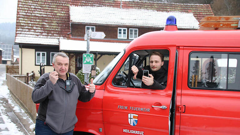 Mitten in Heiligkreuz gibt es zwar einen offiziellen Rettungstreffpunkt (Schild hinten), aber keinen Handy-Empfang: Kommandant Armin Henning (links) hat mit dem Digitalfunkgerät Empfang, während Daniel Niebusch (rechts), Vorsitzender der Wehr, mit dem Handy Pech hat. Foto: Ralf Ruppert       -  Mitten in Heiligkreuz gibt es zwar einen offiziellen Rettungstreffpunkt (Schild hinten), aber keinen Handy-Empfang: Kommandant Armin Henning (links) hat mit dem Digitalfunkgerät Empfang, während Daniel Niebusch (rechts), Vorsitzender der Wehr, mit dem Handy Pech hat. Foto: Ralf Ruppert