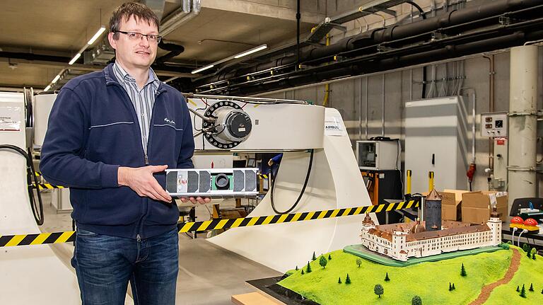 Andreas Nüchter, Professor für Telematik am Lehrstuhl für Robotik und Telematik, mit einem Kleinsatelliten und dem 3-D-Druck der Würzburger Festung auf Grundlage computererfasster Daten.