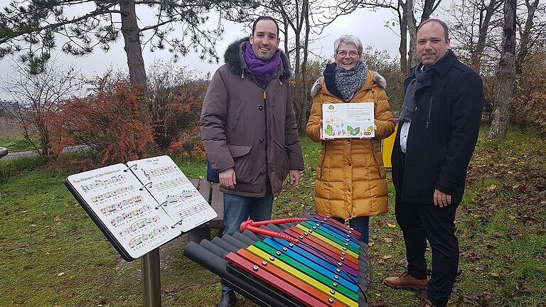 Mitmachstationen bieten Abwechslung auf dem Melodienweg bei Helmstadt, hier Farbklangstäbe und ein Outdoor-Musikbuch mit bekannten Liedern. Nun überreichte (von links) Bürgermeister Tobias Klembt das Förderschild an Andrea Dinkel und Sebastian Kinner vom Gesangverein Melomania. Mitmachstationen bieten Abwechslung auf dem Melodienweg bei Helmstadt, hier Farbklangstäbe und ein Outdoor-Musikbuch mit bekannten Liedern. Nun überreichte (von links) Bürgermeister Tobias Klembt das Förderschild an Andrea Dinkel und Sebastian Kinner vom Gesangverein Melomania.