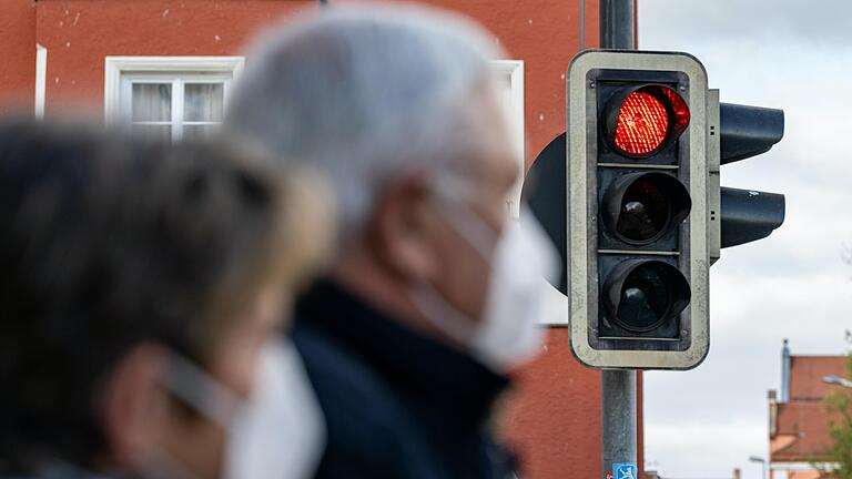 Eine Frau und ein Mann stehen mit einer Maske vor einer Roten Ampel. In vielen Bereichen Bayerns steigen die Infektionen gerade sprunghaft.