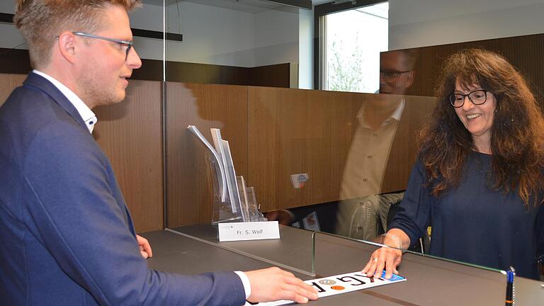 Abteilungsleiter Johannes Büttner posiert für ein Foto am Schalter der Zulassungsstelle. Er wird bedient von Sonja Wolf.