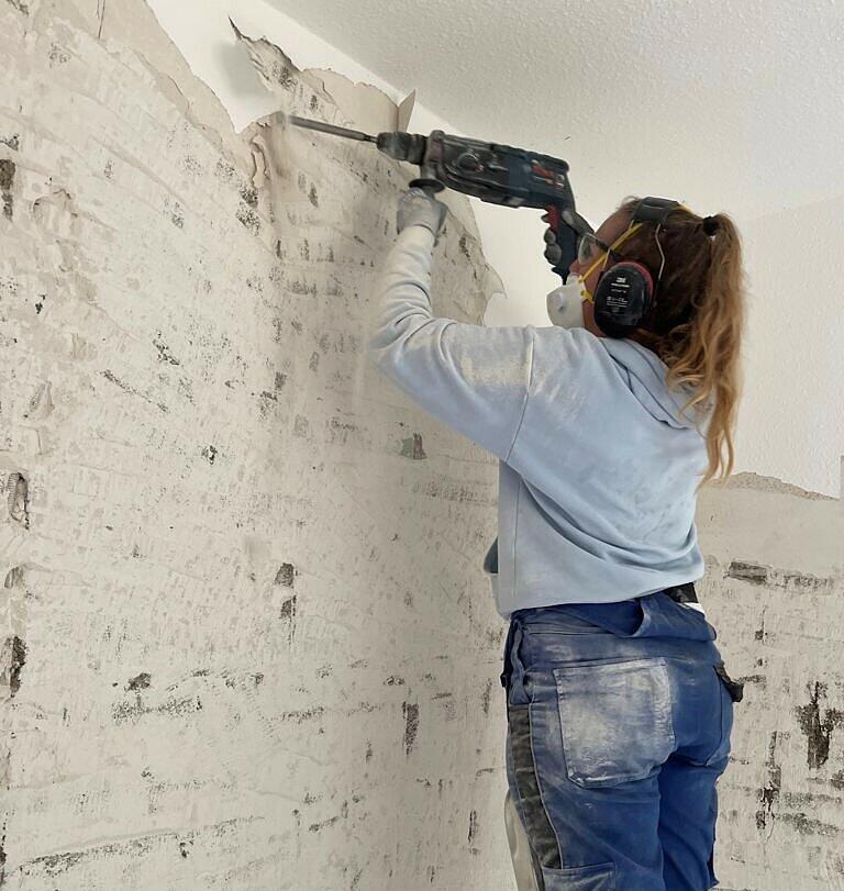 Romy entfernt den Putz von der Wand in einem Haus, das von dem Hochwasser in Mitleidenschaft gezogen wurde. Die Häuser müssen entkernt werden, damit diese bis zum Winter trocknen können.