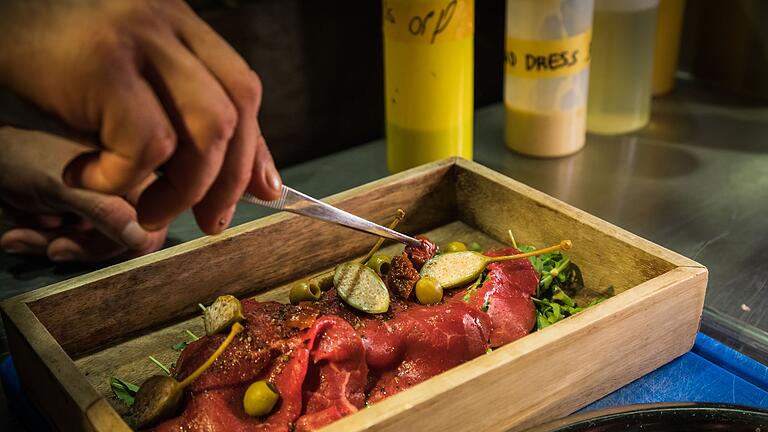 Carpaccio wird im „The Dry Gin and Beef Club” angerichtet - Die Carpaccio-Scheiben werden auf dem Rucola-„Gebirge” angerichtet und mit Oliven, Kapernäpfeln und getrockneten Tomaten getoppt - immer dort, wo der Berg kleine Täler hinterlassen hat. Carpaccio wird im „The Dry Gin and Beef Club” angerichtet - Die Carpaccio-Scheiben werden auf dem Rucola-„Gebirge” angerichtet und mit Oliven, Kapernäpfeln und getrockneten Tomaten getoppt - immer dort, wo der Berg kleine Täler hinterlassen hat.