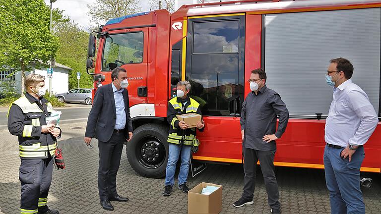 Bürgermeister Jürgen Götz (2.v.l.)  freut sich als oberster Dienstherr der Floriansjünger mit dem 1. Feuerwehrkommandanten Robert Röhm (Bildmitte) und dem stellvertretenden Feuerwehrvereinsvorsitzenden Werner Hess (links) über die Spende von 120 FFP2-Masken und 48 Desinfektionsfläschchen, die Pascal Ritter (2.v.r.)  und Philipp Möller (rechts) von der Marketingabteilung der Würzburger Firma Flyeralarm übergaben. Dazu stehen sie vor dem neuen Löschfahrzeug der Wehr.