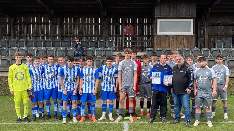 Auf dem Foto sind die Mannschaften von der (SG) SV Viktoria Weigenheim (graue Spielkleidung) und der (SG) TG Höchberg (blaue Spielkleidung) zu sehen. Vorne stehen mit schwarzer Jacke BFV-Kreis-Jugendleiter Claus Höpfner und links daneben der Weigenheimer Coach Andreas Stegmüller.