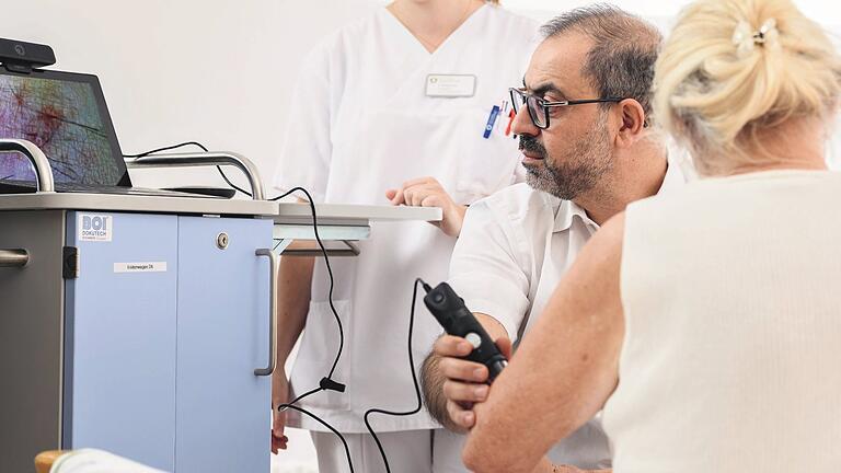 Visite am Rhön-Klinikum: Dr. Hassan Soda, Leitender Arzt der Akut Neurologie II/Stroke Unit und Intensivmedizin am Campus Bad Neustadt untersucht eine Patientin und steht dabei im direkten Kontakt mit den Experten vom Uniklinikum Marburg.