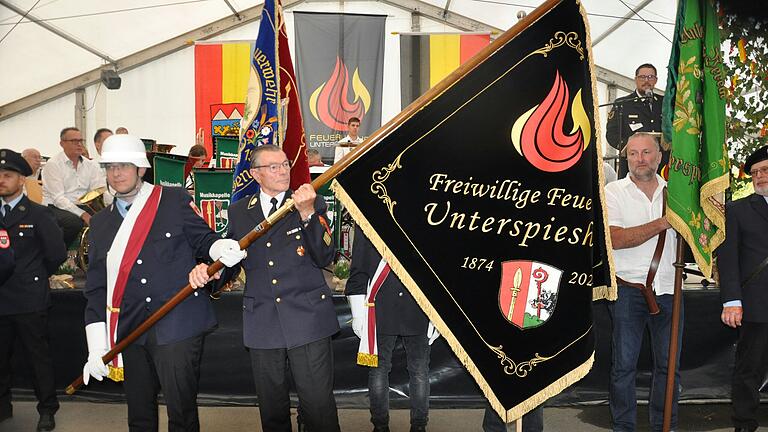 Ehrenmitglied Georg Seufert, Pate der Fahne der Freiwilligen Feuerwehr Unterspiesheim, hält die enthüllte Fahne. Sie zeigt auf der Vorderseite das Ortswappen von Unterspiesheim und die Flamme, das Logo Feuerwehr. Das Wappen und die Flamme sollen die Verbindung zwischen Vergangenheit und Zukunft symbolisieren. Ehrenmitglied Georg Seufert, Pate der Fahne der Freiwilligen Feuerwehr Unterspiesheim, hält die enthüllte Fahne. Sie zeigt auf der Vorderseite das Ortswappen von Unterspiesheim und die Flamme, das Logo Feuerwehr. Das Wappen und die Flamme sollen die Verbindung zwischen Vergangenheit und Zukunft symbolisieren.