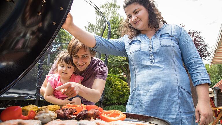 Eine Familie am Grill       -  Sicherer grillen: Damit keine potenziell krebserregende Stoffe entstehen, sollte Fleisch nicht zu lange direkt über der Glut garen.