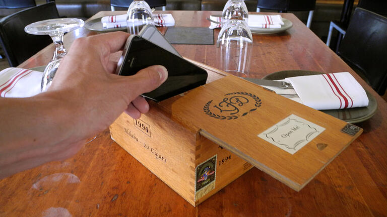 Handyverbot im Restaurant: Das sagen Würzburger Gastronomen - Ein Gast legt sein Handy in eine dafür vorgesehene Zigarrenkiste im Restaurant Hearth in New York. (Symbolbild) Handyverbot im Restaurant: Das sagen Würzburger Gastronomen - Ein Gast legt sein Handy in eine dafür vorgesehene Zigarrenkiste im Restaurant Hearth in New York. (Symbolbild)
