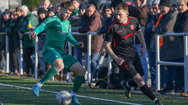 Dick eingemummelt verfolgen Zuschauerinnen und Zuschauer die Bayernliga-Partie zwischen dem TSV Abtswind und dem ASV Neumarkt. In dieser Szene führt Egor Zelenskiy (links) den Ball gegen Selim Mjaki vom ASV Neumarkt. Die Begegnung endete torlos.