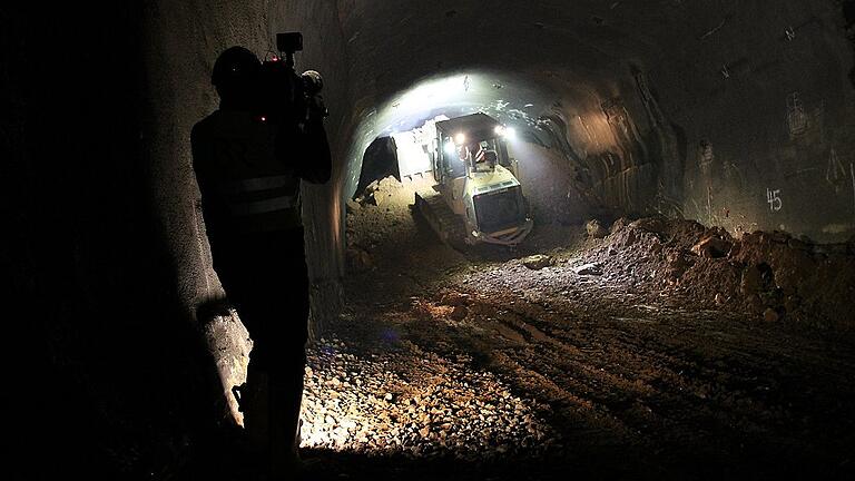 Eine Raupe schiebt das Verfüllmaterial in den Tunnel, ein Kameramann filmt den Vorgang.