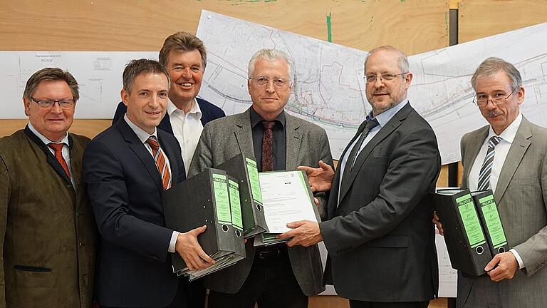 Die Ordner für das Planfeststellungsverfahren &bdquo;Ortsumgehung Hafenlohr mit integrierter Hochwasserschutzmaßnahme&ldquo; wurden übergeben. Im Bild (von links): Staatssekretär Gerhard Eck, Bürgermeister Thorsten Schwab, stellvertretender Landrat Harald Schneider, Norbert Böhm (Regierung Unterfranken), Michael Fuchs (Staatliches Bauamt) und Herbert Walter (Wasserwirtschaftsamt).