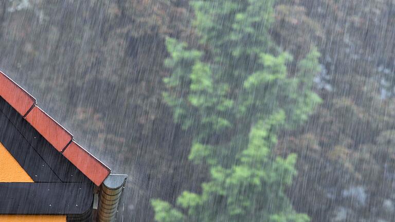 Regen fällt auf ein Hausdach       -  Teils wird es sehr nass in Deutschland. (Archivbild)