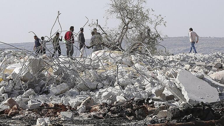 Nach Angriff auf IS-Anführer Al-Bagdadi in Syrien       -  Menschen stehen auf Trümmern eines Hauses in der Nähe des Dorfes Barisha in der Provinz Idlib nach einer Militäroperation der USA gegen Al-Baghdadi, Anführer der Terrormiliz Islamischer Staat. Al-Baghdadi ist bei dem Angriff umgekommen.