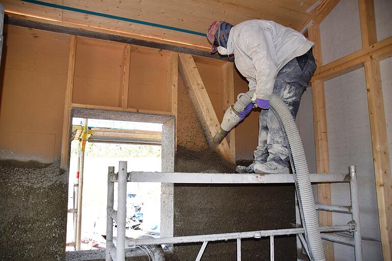 Mit einem Schlauch sprüht ein Arbeiter das Gemisch aus Hanfschäben, Kalk und Wasser auf das Gefache der Holzständer.