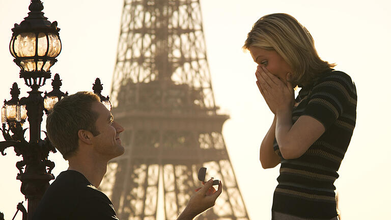 medium shot of a young adult couple as the man proposes in front of the eiffel tower in paris       -  Der Heiratsantrag ist einer der wichtigsten Momente im Leben eines Paares. Wie aber soll dieser aussehen?