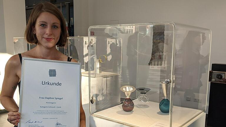 Daphne Spiegel hat den hessischen Gestaltungspreis gewonnen. Die junge Designerin mit fränkischen Wurzeln, die an der Staatlichen Zeichenakademie in Hanau als Beste ihren Abschluss zur Gold- und Silberschmiedemeisterin sowie Produktdesignerin absolviert hat, sicherte sich mit ihrem künstlerisch aus Glas und Silber gestalteten Vasenobjekt den ersten Preis in der Kategorie 'Schmuck und Gerät'.