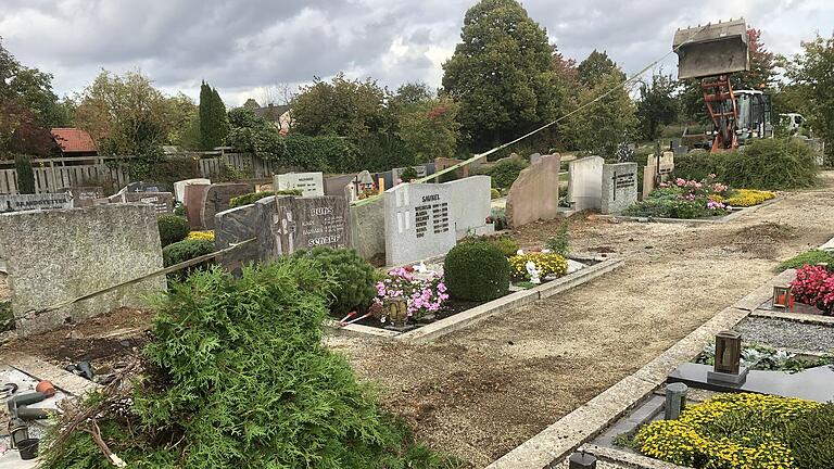 Die Thuja-Hecken zwischen den Grabsteinen auf dem Gerolzhöfer Friedhof werden derzeit gerodet. Ein Radlader zieht die Pflanzen über lange Gurte aus dem Erdreich. Die Thuja-Hecken zwischen den Grabsteinen auf dem Gerolzhöfer Friedhof werden derzeit gerodet. Ein Radlader zieht die Pflanzen über lange Gurte aus dem Erdreich.