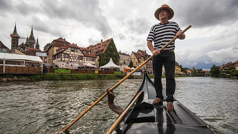 Ein Gondolieri rudert auf der Regnitz entlang der Bamberger Altstadt. Die oberfränkische Stadt vermittelt mit ihrer historischen Häuserkulisse direkt am Fluss mediterranes Flair.