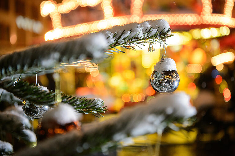 Bunte Christbaumkugeln hängen 2017 an einem verschneiten Weihnachtsbaum vor dem Kinderkarussell auf dem Würzburger Weihnachtsmarkt.&nbsp;