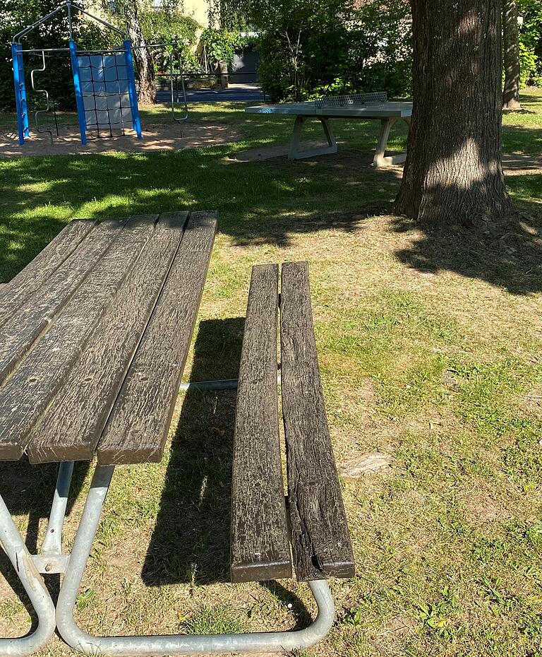 Diese Bank auf dem Spielplatz 'An den Birken' ist ziemlich abgenutzt. Im Hintergrund ist das halbhohe Geländer zu sehen, das Kindern keinen Schutz vor freilaufenden Hunden bietet und sie nicht daran hindert, auf die Straße zu rennen.