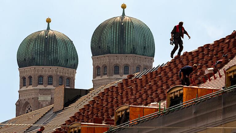 Dachdecker bei der Arbeit in München       -  Dachdecker auf einem Hausdach vor der Kulisse der Münchner Frauenkirche