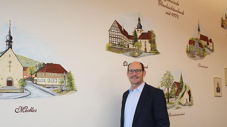 Dieter Muth steht im Konferenzzimmer des Rathauses der Gemeinde Oberleichtersbach. Die fünf Gemeindeteile sind an der Wand verewigt.  Foto: Julia Raab       -  Dieter Muth steht im Konferenzzimmer des Rathauses der Gemeinde Oberleichtersbach. Die fünf Gemeindeteile sind an der Wand verewigt.  Foto: Julia Raab