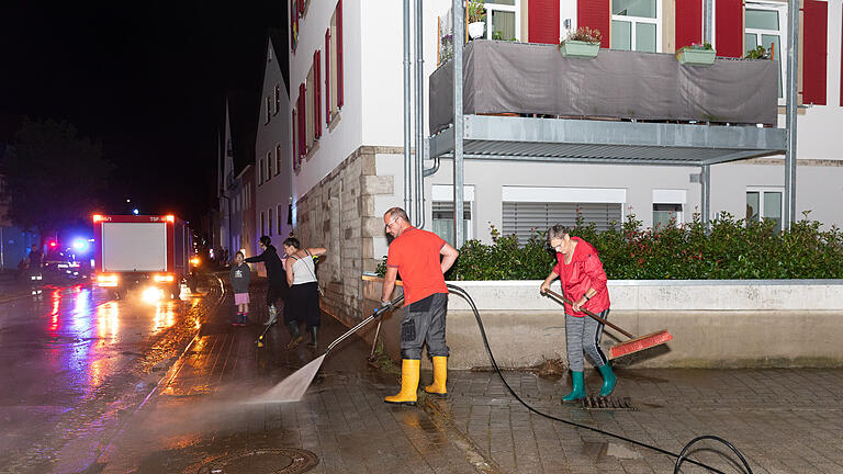 Sturzflut in Reichenberg: Nach dem Starkregen am Samstag (03.08.24) hat eine Sturzflut Reichenberg im Landkreis Würzburg heimgesucht. Am Abend schoss das Wasser durch die Bahnhofstraße, die Hauptverkehrsader des Ortes. Menschen versuchen, Wasser und Schlamm Herr zu werden.