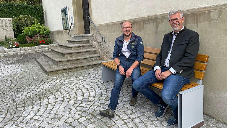 Auf dem Bild Bürgermeister Bernhard Weidner (rechts) und Dirk Wiesner auf der neuen Sitzbank an der Gramschatzer Cyriakus-Kirche.