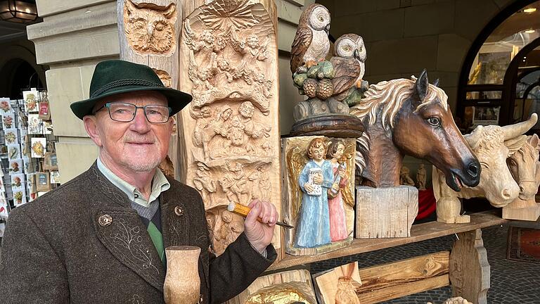 Holzschnitzer Hans-Joachim Seitfudem vor einer Krippe im Baustamm, die er letztes Jahr in Würzburg geschnitzt hat.