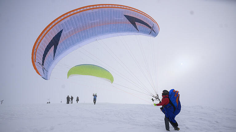 Schnee in der Rhön       -  Wintereinbruch in der Rhön: Zwei Paraglider üben am Sonntag (11.12.22) zwischen Radom und Fliegerdenkmal an der Wasserkuppe bei Poppenhausen. Bei Schneefall und eisiger Kälte zieht es am Sonntag zahlreiche Touristen in die Rhön.