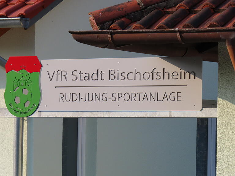 Mit der feierlichen Übergabe wurde der Abschluss der Arbeiten und die Umbenennung in Rudi-Jung-Sportanlage in Bischofsheim gefeiert. Über dem Eingangstor prangt der neue Name des Geländes: Rudi-Jung-Sportanlage.