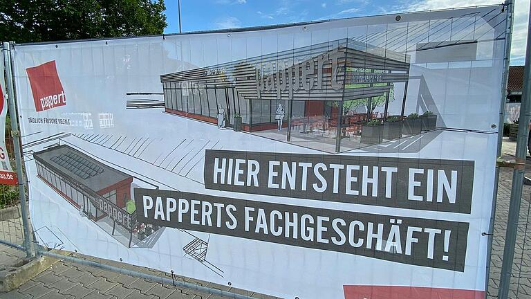 Die Bäckerei Pappert hat das Baugelände auf dem Aldi-Parkplatz abgesperrt und zeigt auf einem Banner, wie das neue Bäckerei-Fachgeschäft in Mellrichstadt aussehen wird.