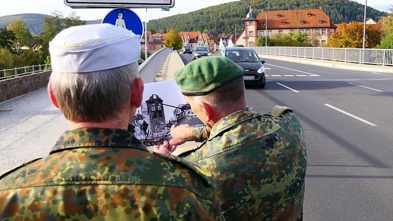 Oberstleutnant Mario Cremer zeigt Brigadegeneral Michael Matz die Stelle, an der US-Panzer vor der Brücke in Gemünden abgeschossen wurde. Die gesprengte Brücke (links an der aus Sandstein gemauerten Brüstung zu erkennen) wurde nach dem Krieg wiede...       -  Oberstleutnant Mario Cremer zeigt Brigadegeneral Michael Matz die Stelle, an der US-Panzer vor der Brücke in Gemünden abgeschossen wurde. Die gesprengte Brücke (links an der aus Sandstein gemauerten Brüstung zu erkennen) wurde nach dem Krieg wiederaufgebaut und ist heute eine Fußgängerbrücke, daneben ist eine neue breitere Straßenbrücke.