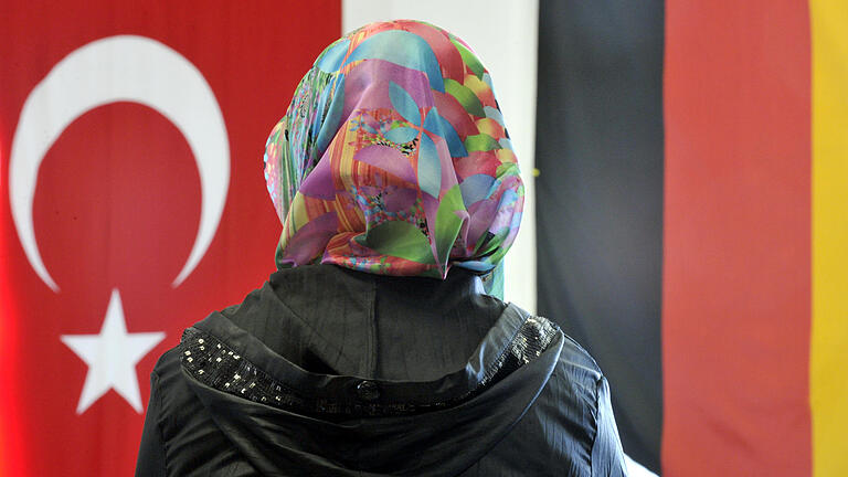 DITIB-Moschee       -  ARCHIV - Ein Frau mit Kopftuch sitzt am 22.05.2010 in der DITIB-Moschee im hessischen Friedberg vor einer türkischen und einer deutschen Fahne. Foto: Boris Roessler/dpa