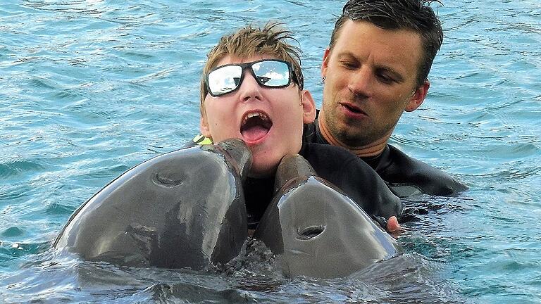 Tommi Adams im Wasser der Lagune des Delfintherapiezentrums auf der Karibikinsel Curaçao mit Therapeut Matthias Treu und den beiden Delfinen Kanoa und Nubia.