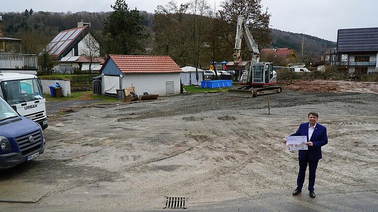 Auf diesem freien Platz zwischen Dorfladen, neuer katholischer Kirche und evangelischer Kirche soll das Ärztehaus mit Dorfladen und Gemeindesaal entstehen. Bürgermeister Johannes Wagenpfahl zeigt dazu einen ersten Entwurf Auf diesem freien Platz zwischen Dorfladen, neuer katholischer Kirche und evangelischer Kirche soll das Ärztehaus mit Dorfladen und Gemeindesaal entstehen. Bürgermeister Johannes Wagenpfahl zeigt dazu einen ersten Entwurf